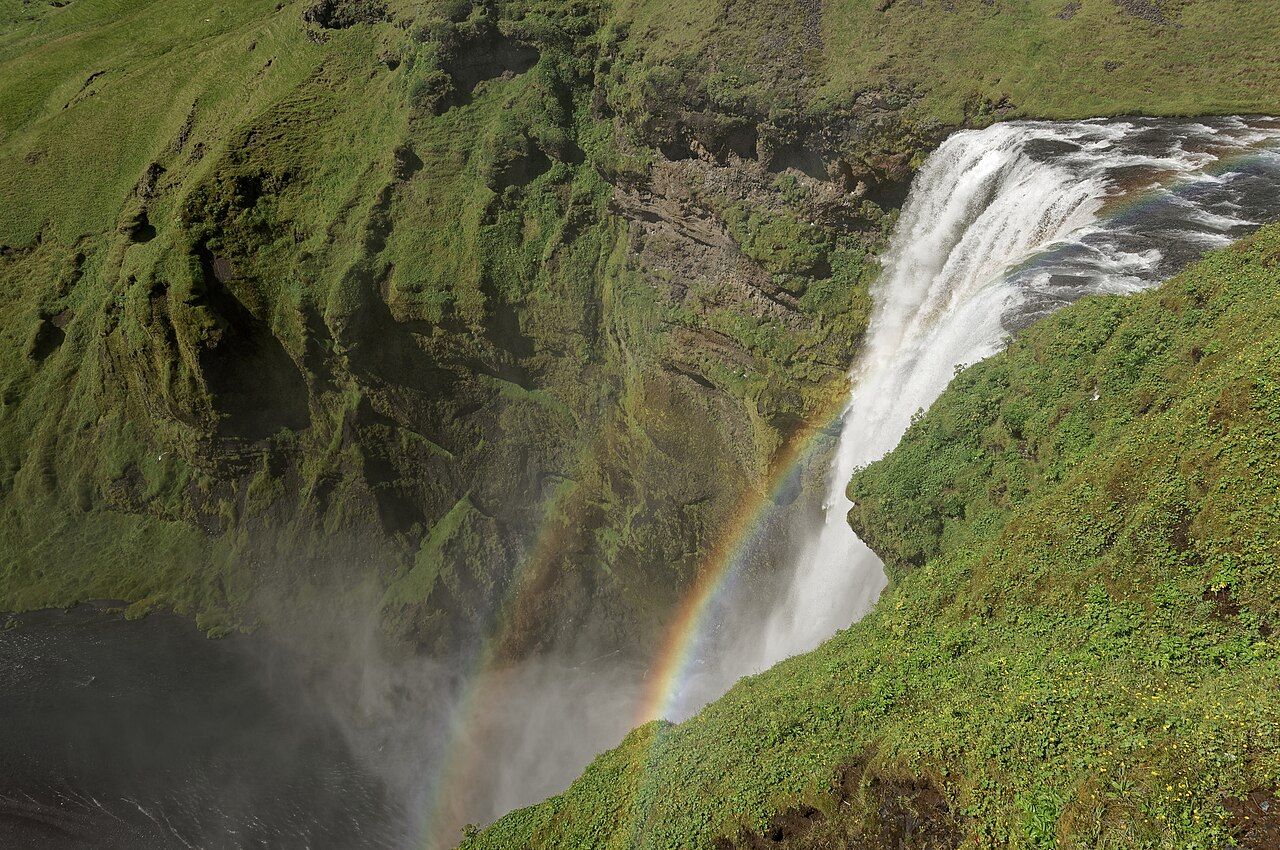 Skógafoss, a wide waterfall falling over a cliff into a green valley on Iceland's south coast