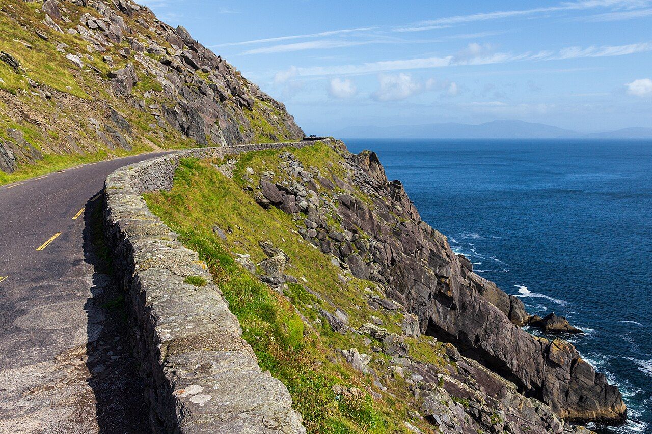 A narrow coast road with a low stone wall above dark cliffs and the Atlantic on Slea Head Drive, County Kerry