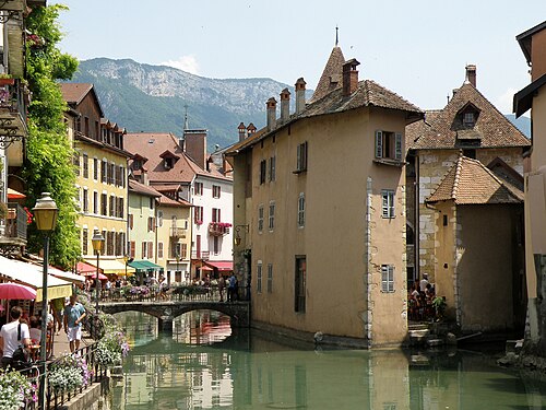 The Palais de l'Isle and old town houses beside a green canal in Annecy, with a mountain behind