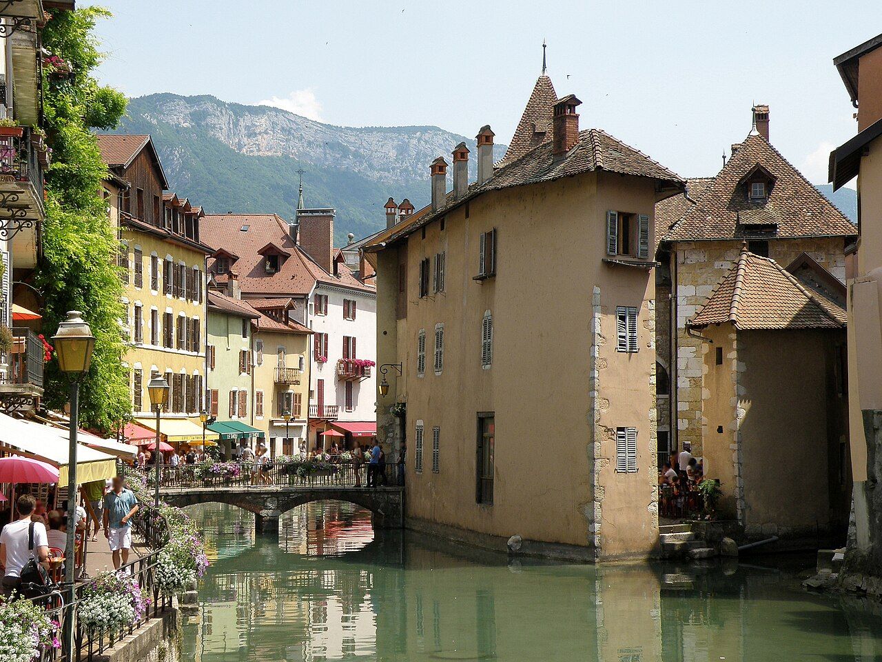The Palais de l'Isle and old town houses beside a green canal in Annecy, with a mountain behind