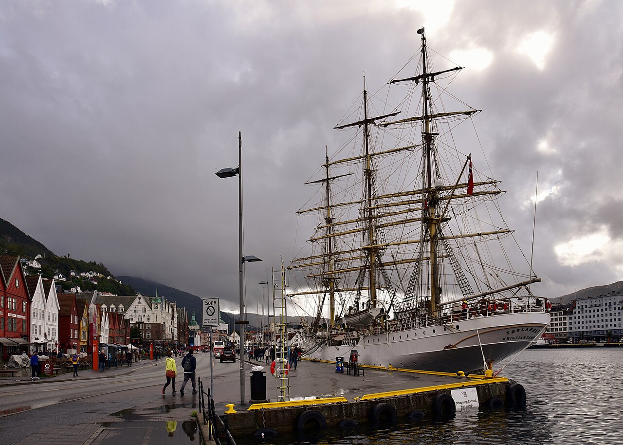 The wooden gabled warehouses of Bryggen on the Bergen waterfront, with the harbor bay of Vågen and a tall ship beside them