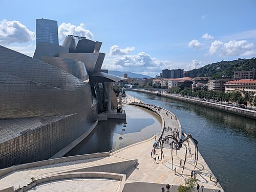 The Guggenheim Museum Bilbao beside the Nervión river, with its curved titanium walls and the city behind