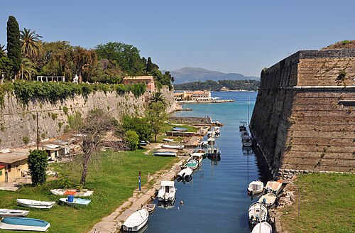 The Old Fortress wall beside a narrow sea channel with small boats, in Corfu Town