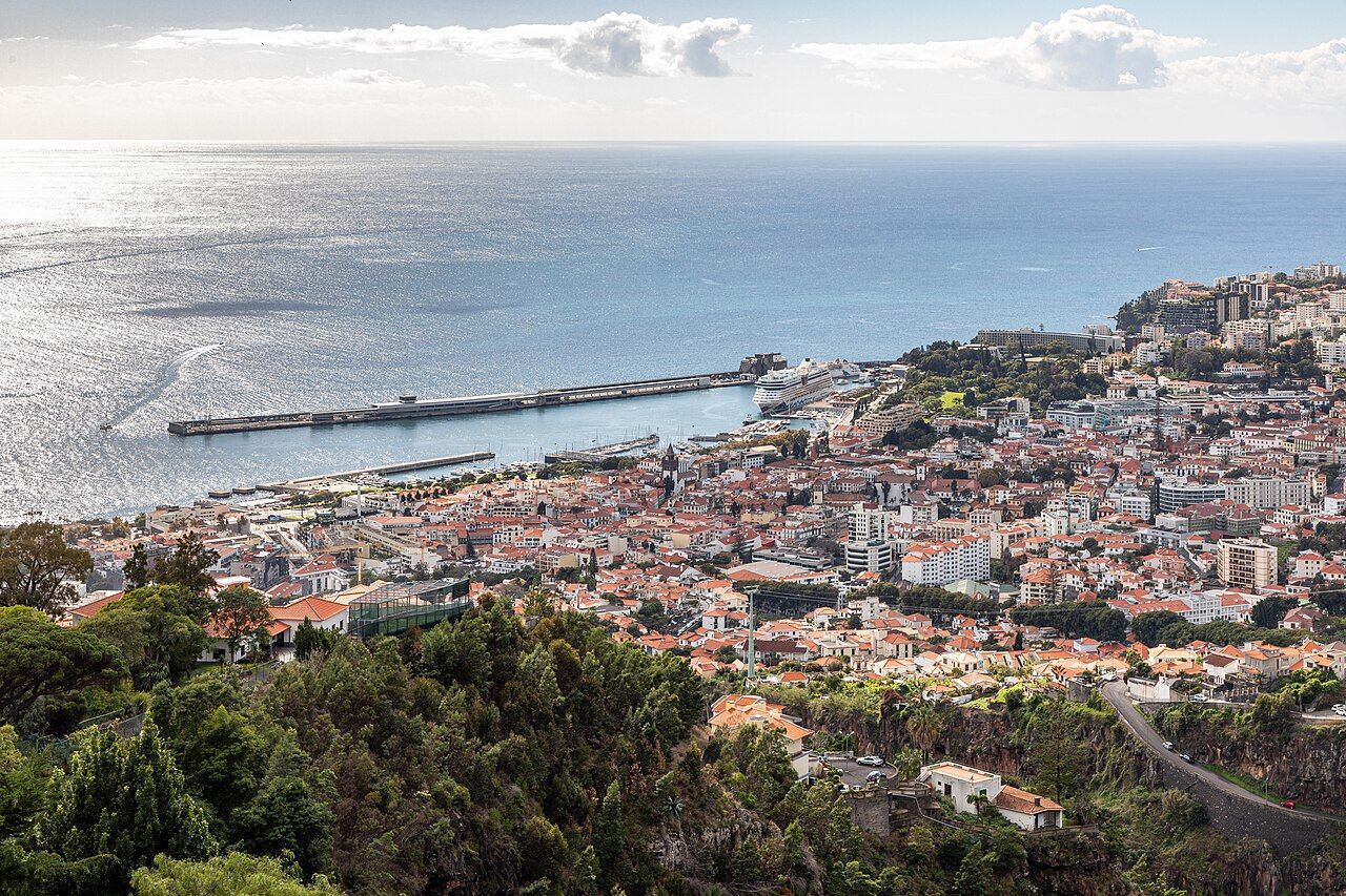 Funchal's harbor, breakwater and red-roofed town seen from the hillside above, with the Atlantic beyond