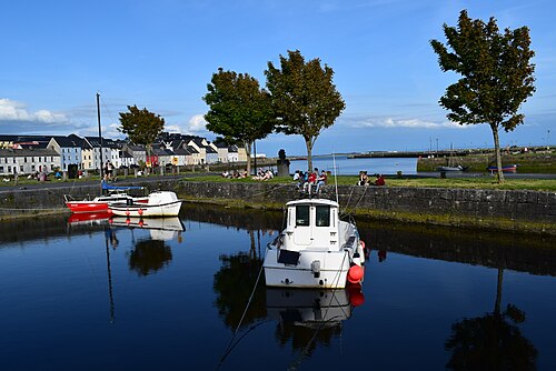 A small boat moored in the Claddagh basin in Galway, with the painted houses of the Long Walk along the far bank