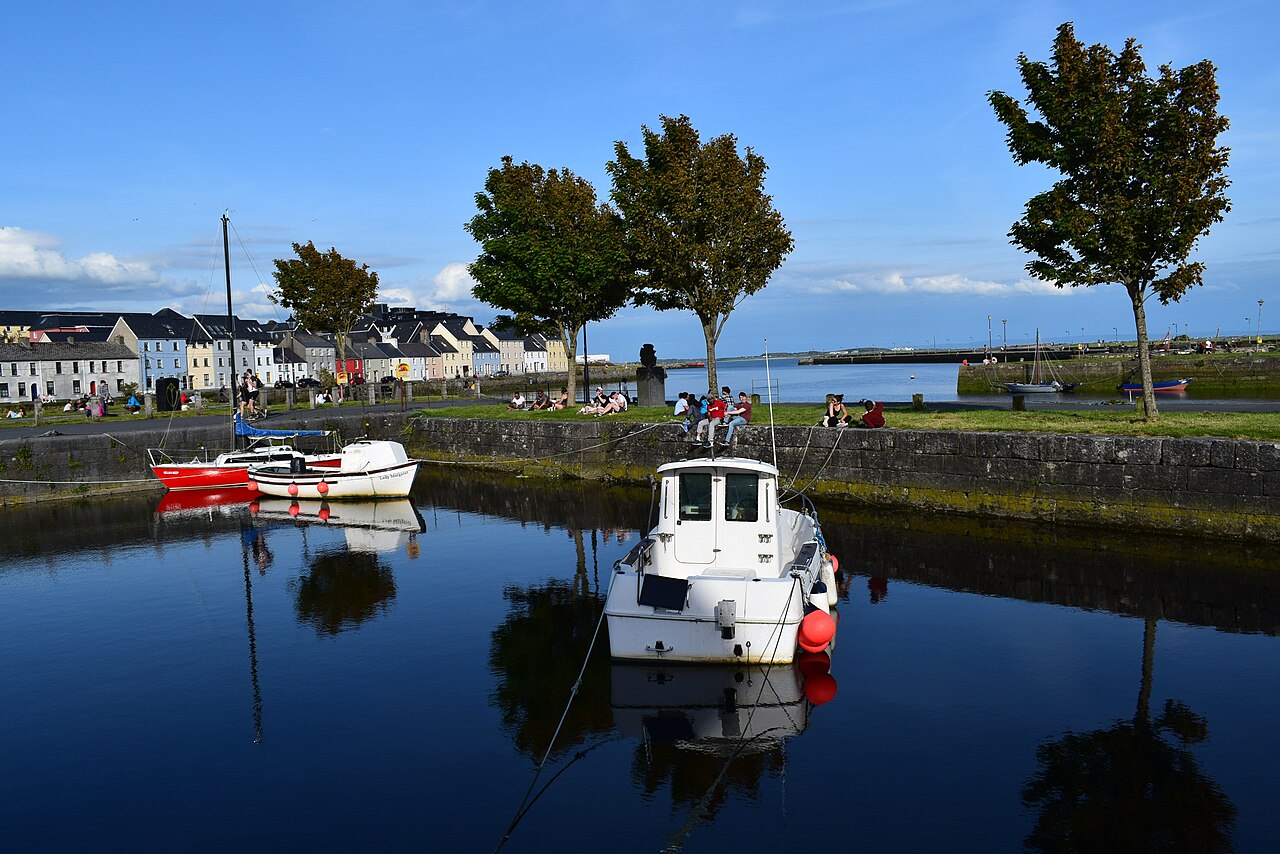 A small boat moored in the Claddagh basin in Galway, with the painted houses of the Long Walk along the far bank