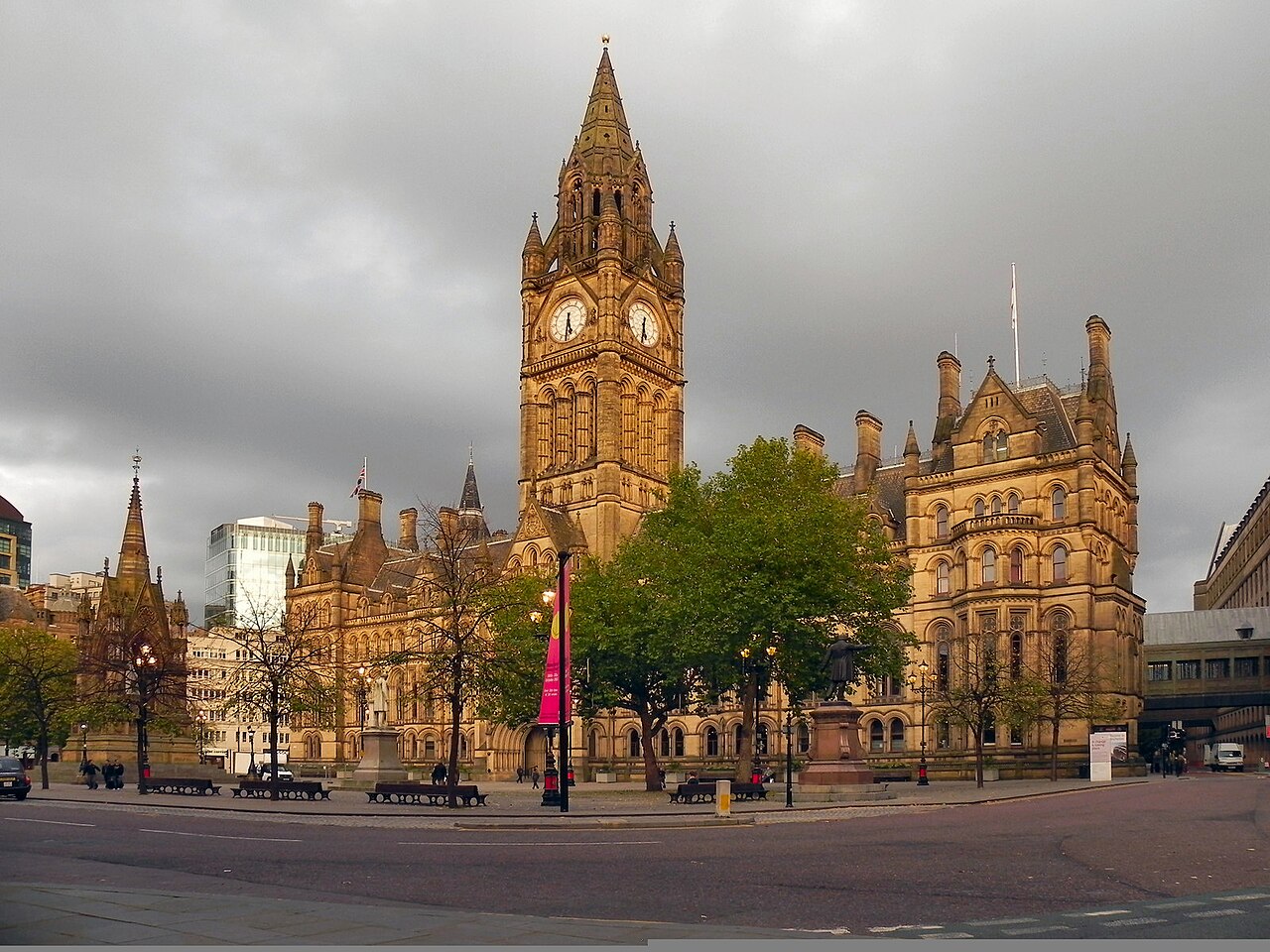 The Gothic Revival Manchester Town Hall with its tall clock tower, seen across a square with trees under a dark, cloudy sky