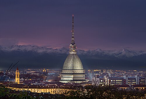 The Mole Antonelliana in Turin lit up at night, with the Alps behind