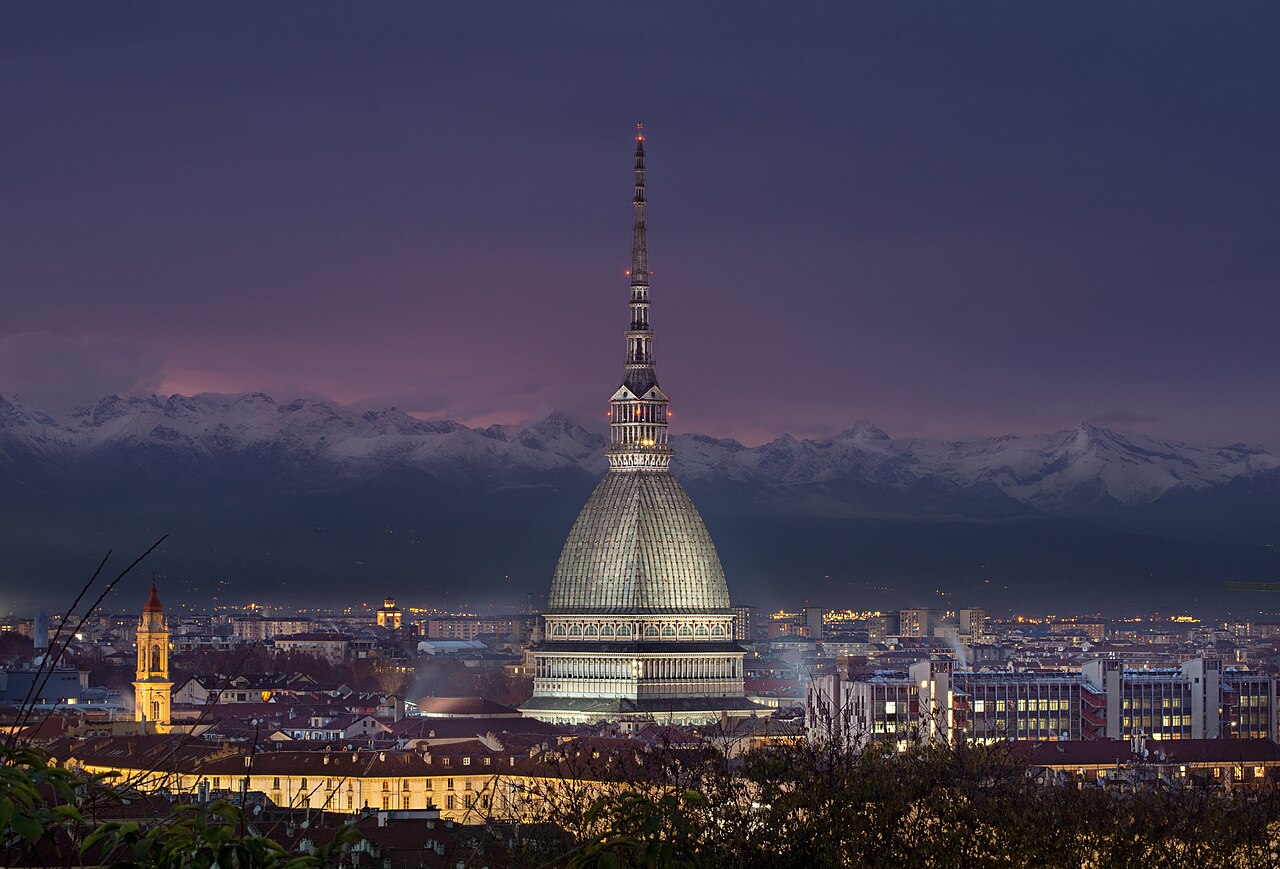 The Mole Antonelliana in Turin lit up at night, with the Alps behind