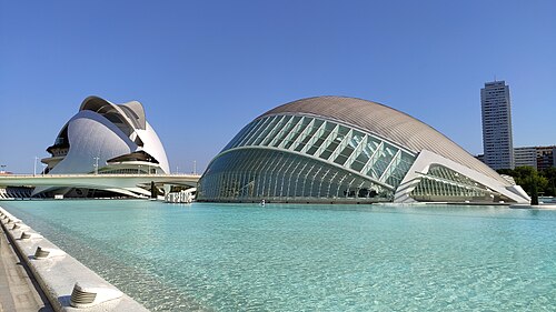 The Palau de les Arts and the Hemisfèric beside a pale turquoise pool in the City of Arts and Sciences, under a clear blue sky