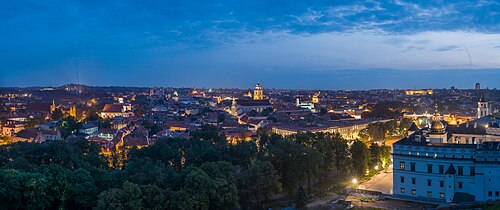 The rooftops and church towers of Vilnius Old Town at dusk, seen from above with the lights coming on